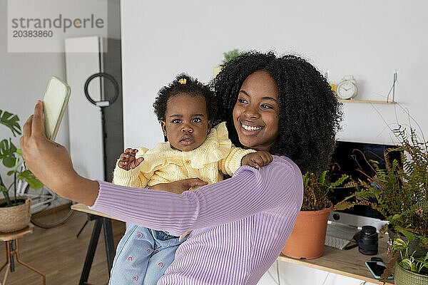 Happy mother carrying daughter taking selfie with smart phone at home