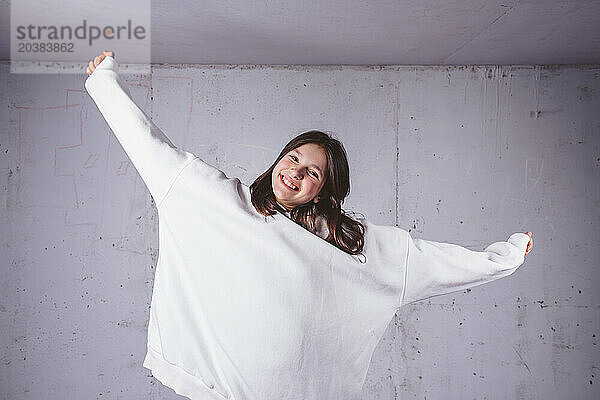 Happy girl in white hoodie with arms outstretched in front of gray cement background