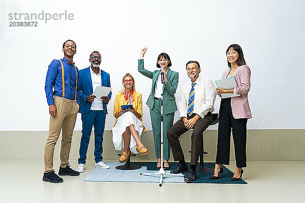 Businesswoman holding fist amidst colleagues near wall at office