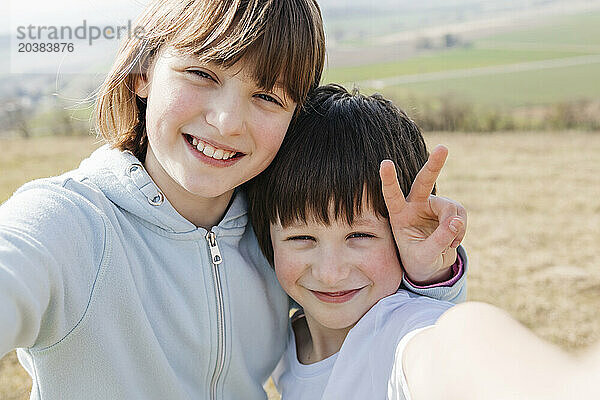 Smiling girl showing peace sign and taking selfie with brother