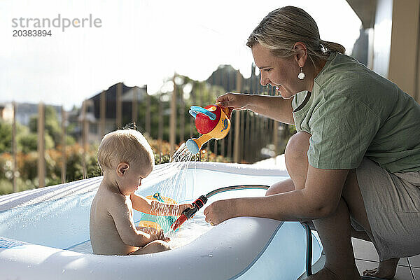 Smiling mother bathing son in inflatable tub at balcony