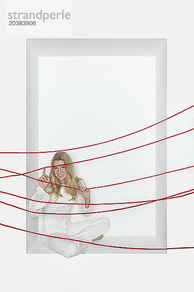 Teenage girl with red thread sitting in alcove against white background