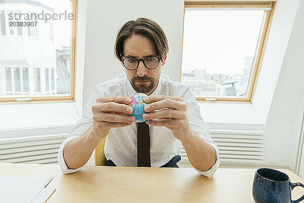 Confident businessman looking at globe in office