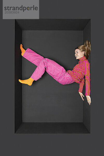 Teenage girl with legs up inside alcove over black background