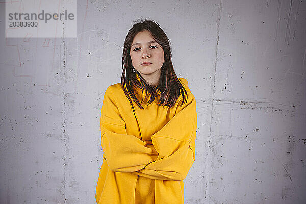 Confident girl in yellow hoodie posing in front of gray background