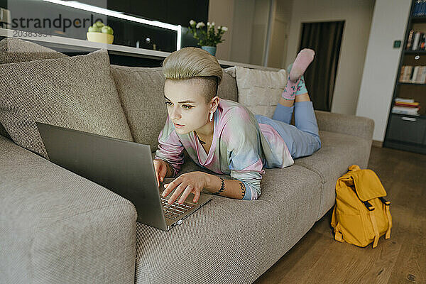 Young woman using laptop lying down on sofa at home