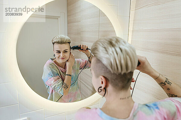 Young hipster woman trimming hair in bathroom at home