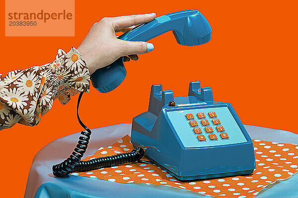 Hand of woman picking up telephone receiver against orange background