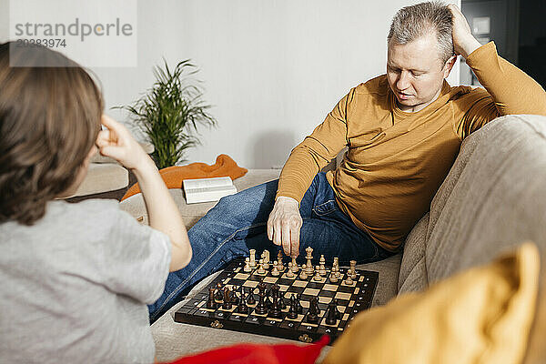 Father and son playing chess on sofa at home