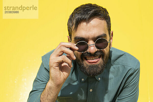 Cheerful man wearing sunglasses against yellow background