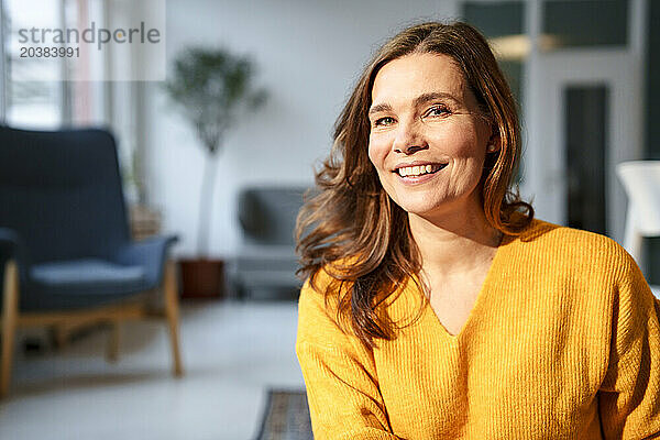 Smiling mature woman under sunlight in living room at home