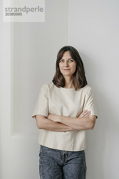 Confident woman with arms crossed in front of wall