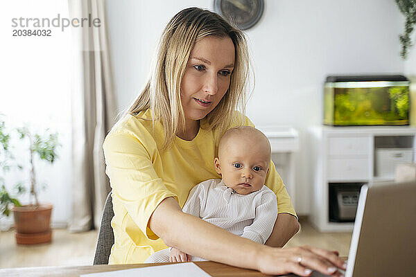 Blond businesswoman using laptop sitting with son at table