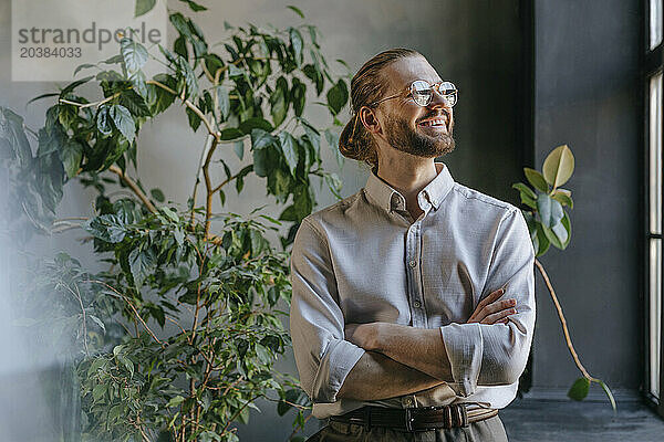 Happy businessman standing with arms crossed in office