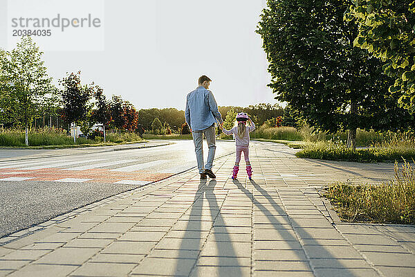 Man holding hand of daughter doing roller skating on sidewalk