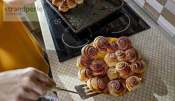 Senior woman putting sweet dough buns on plate in kitchen at home