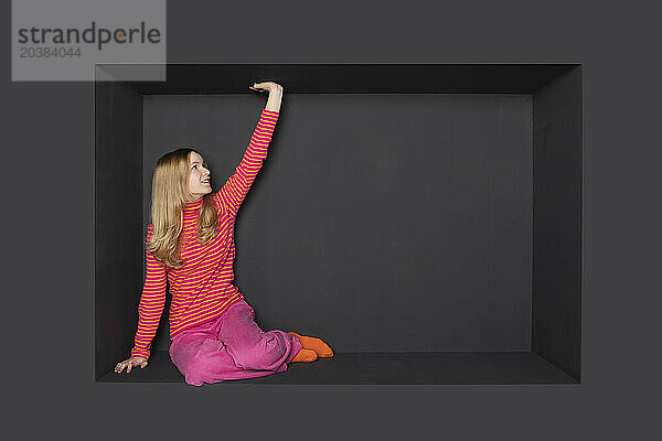 Blond teenage girl touching alcove against black background