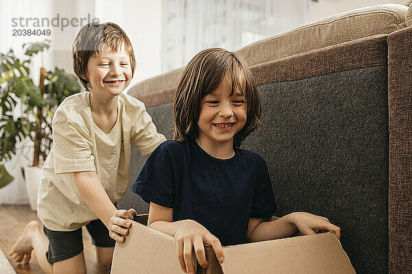 Happy boy pushing brother sitting in cardboard box at home