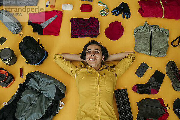 Happy woman lying near travel kit against yellow background
