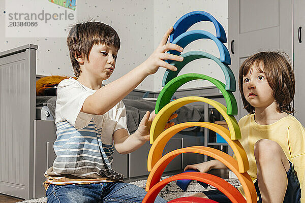 Brothers building pyramid with colorful rainbow toys at home