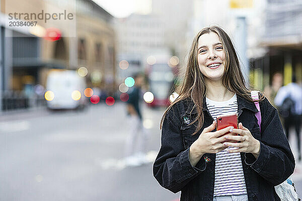 Happy young woman standing with smart phone in city