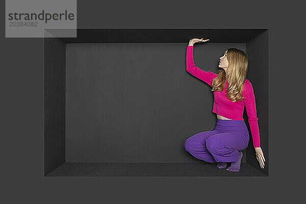 Blond teenager squatting in alcove over black background