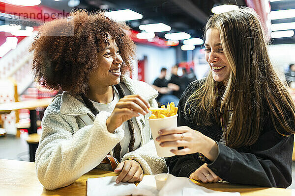 Happy young friends sharing french fries in cafe