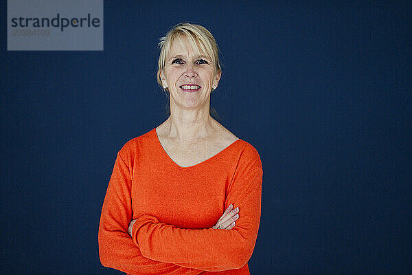 Smiling businesswoman standing with arms crossed against navy blue background