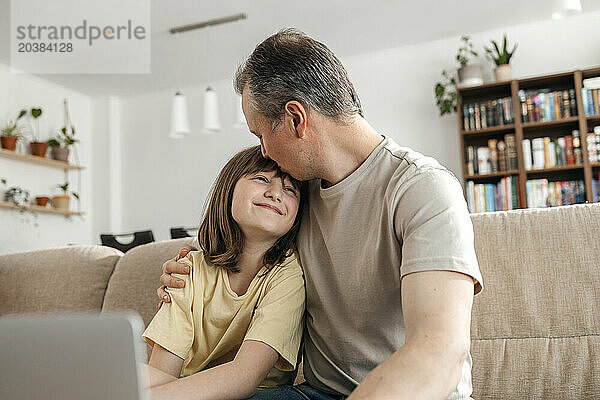 Man kissing daughter on forehead at home