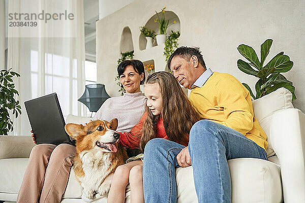 Grandparents with granddaughter and pet dog on sofa at home