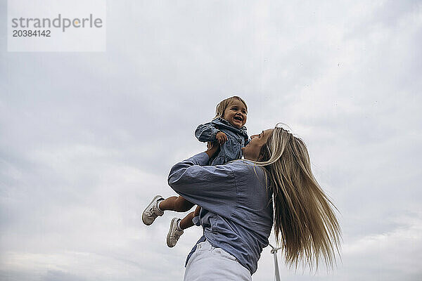 Happy woman holding daughter aloft under sky