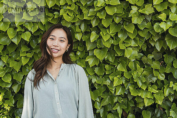 Smiling woman standing in front of green hedge