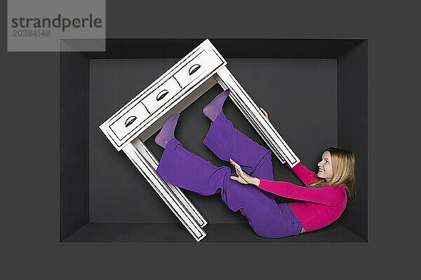 Teenage girl with table in alcove by black background