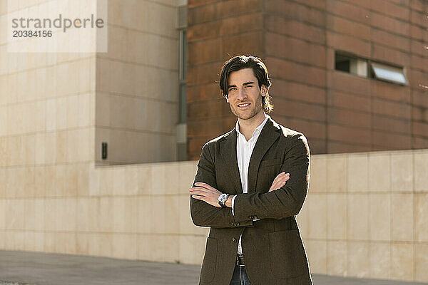 Smiling businessman with arms crossed in front of wall