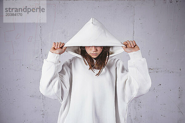 Girl wearing white hoodie in front of gray cement background