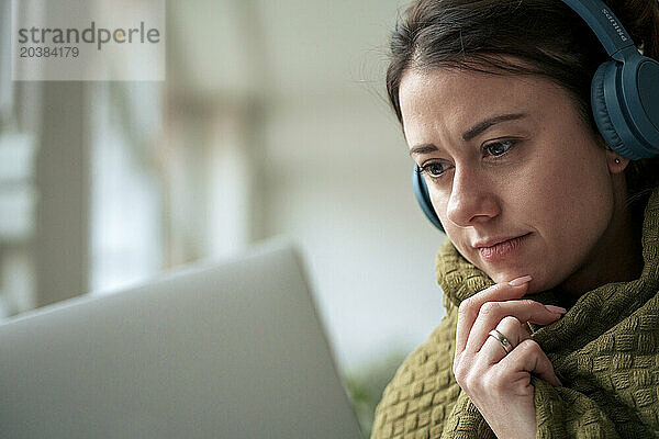 Woman wrapped in blanket looking at laptop