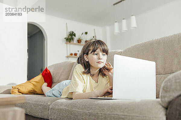 Girl lying down and studying on laptop at home