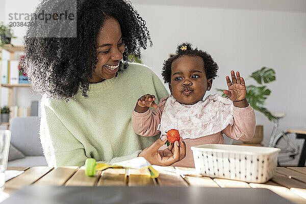 Happy mother feeding strawberry to daughter at home