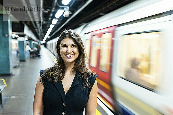 Smiling young woman standing near moving subway train