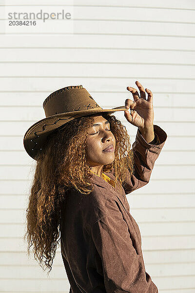 Young woman with eyes closed wearing jacket and cowboy hat on sunny day