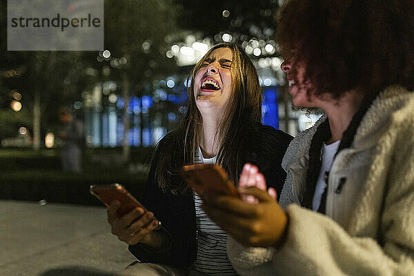Cheerful young friends with smart phones enjoying at night
