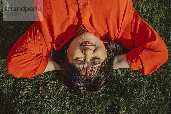 Smiling mature woman with hands behind head lying on grass in back yard
