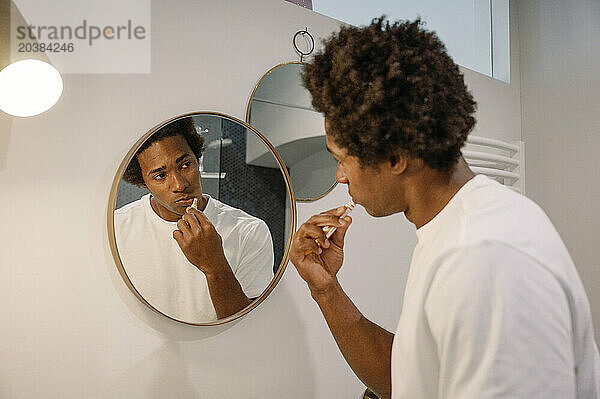 Man brushing teeth looking at mirror in bathroom