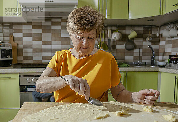 Senior woman preparing pastries with dough in kitchen at home