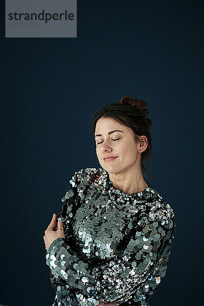 Beautiful woman wearing sequin dress standing with eyes closed against colored background