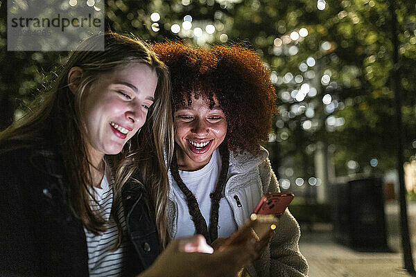 Smiling friends sharing smart phones at night