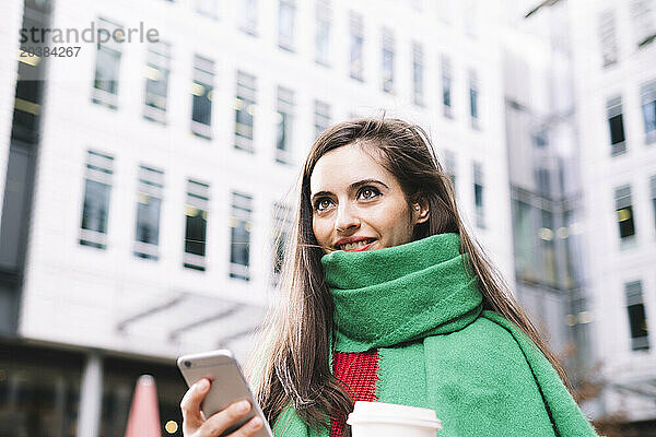 Smiling woman holding smart phone in front of building