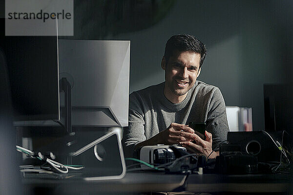 Smiling mature businessman sitting near desktop PC at desk in office