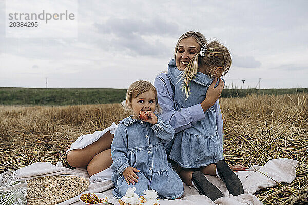 Happy woman enjoying picnic with daughters sitting on blanket over hay