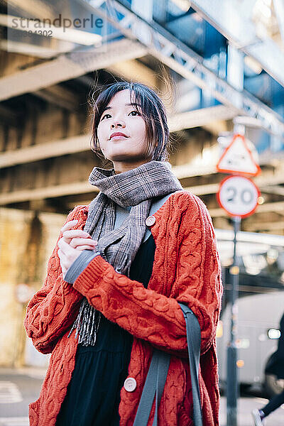 Beautiful young woman standing with hands clasped on street